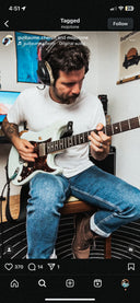 Person playing guitar in a room with a computer screen and posters on the wall.