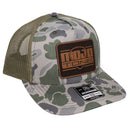 A Mojotone leather patch trucker cap in Bottomland camo isolated on a white background.