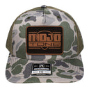 A Mojotone leather patch trucker cap in Bottomland camo isolated on a white background.