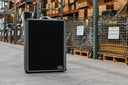 Black speaker in a warehouse setting with pallets and boxes in the background