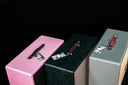 Three jewelry boxes in pink, green, and gray with decorative elements on a black background.