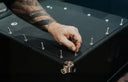 Hand with tattoos placing a silver lock on a black surface