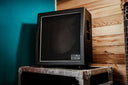 Vintage-style black speaker on a wooden platform against a teal wall